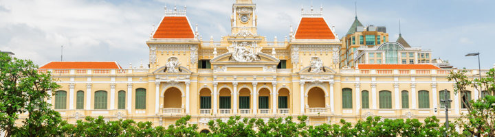Gevel van het Ho Chi Minh City Hall met rode daken en klokkentoren, omringd door groen.