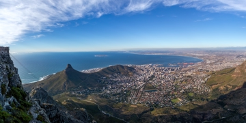 Panoramisch uitzicht vanaf de Tafelberg over Kaapstad, Lion’s Head en de Atlantische kustlijn onder een blauwe lucht.