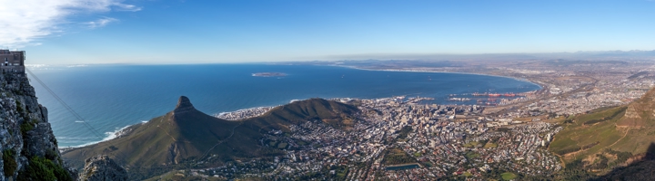 Panoramisch uitzicht vanaf de Tafelberg over Kaapstad, Lion’s Head en de Atlantische kustlijn onder een blauwe lucht.