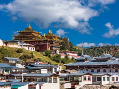 Tibetaans boeddhistisch klooster boven een bergdorp in China, onder een helderblauwe lucht met wolken.