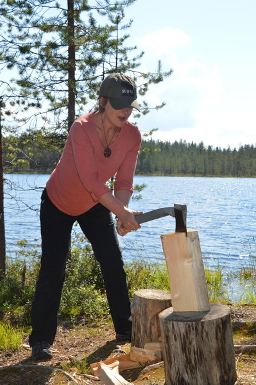 Reiziger hakt hout bij een meer in Lapland, Finland, tijdens een zomerse groepsrondreis.