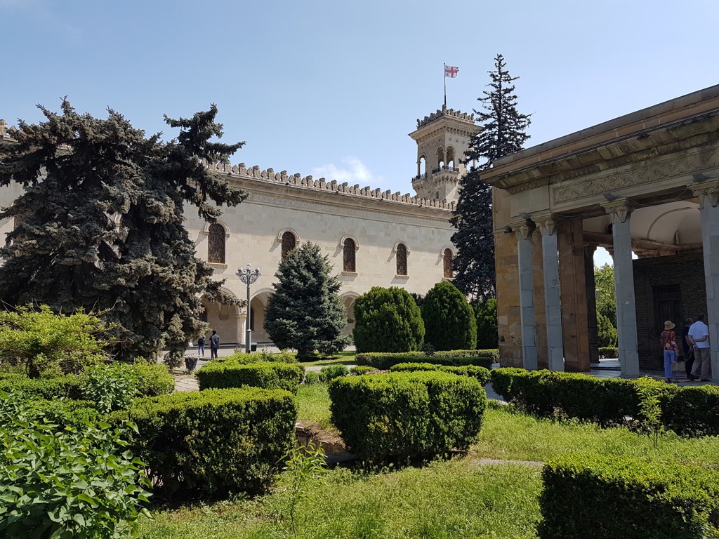 Binnenplaats van een historisch gebouw in Tbilisi met Georgische vlag, omringd door groen en bomen.