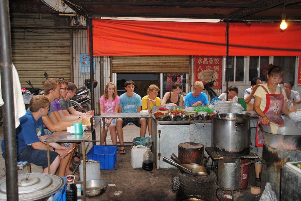 Familiereis China: gezin eet bij een lokale eetkraam met open keuken en rode luifel.
