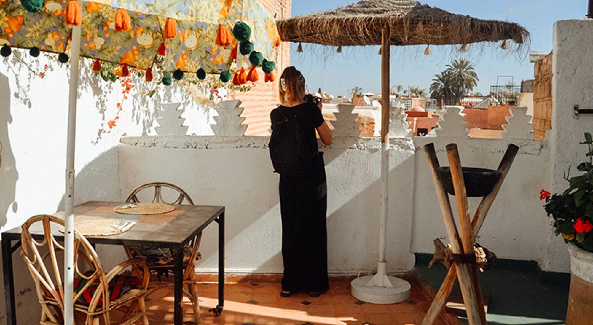 Dakterras Marrakesh Vrouw op dakterras maakt foto van de stad, met parasol, tafel en kleurrijke decoratie.