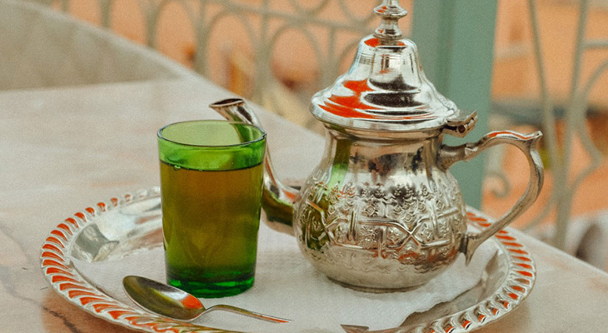 Marokkaanse thee Marokkaanse muntthee in groen glas naast zilveren theepot op dienblad.