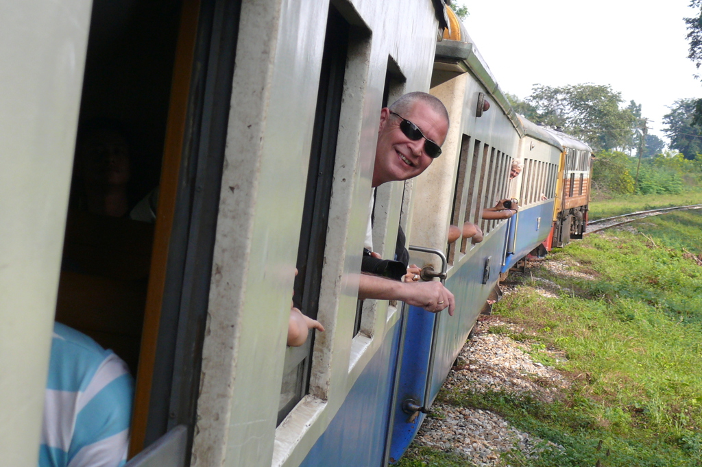 Reiziger leunt uit een rijdende trein tijdens rondreis door Zuid-Thailand.