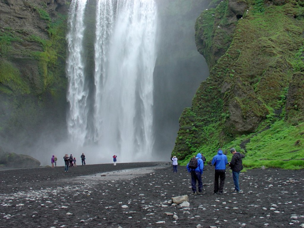 Waterval in IJsland met reizigers op zwart lavazand, tijdens een familiereis IJsland.
