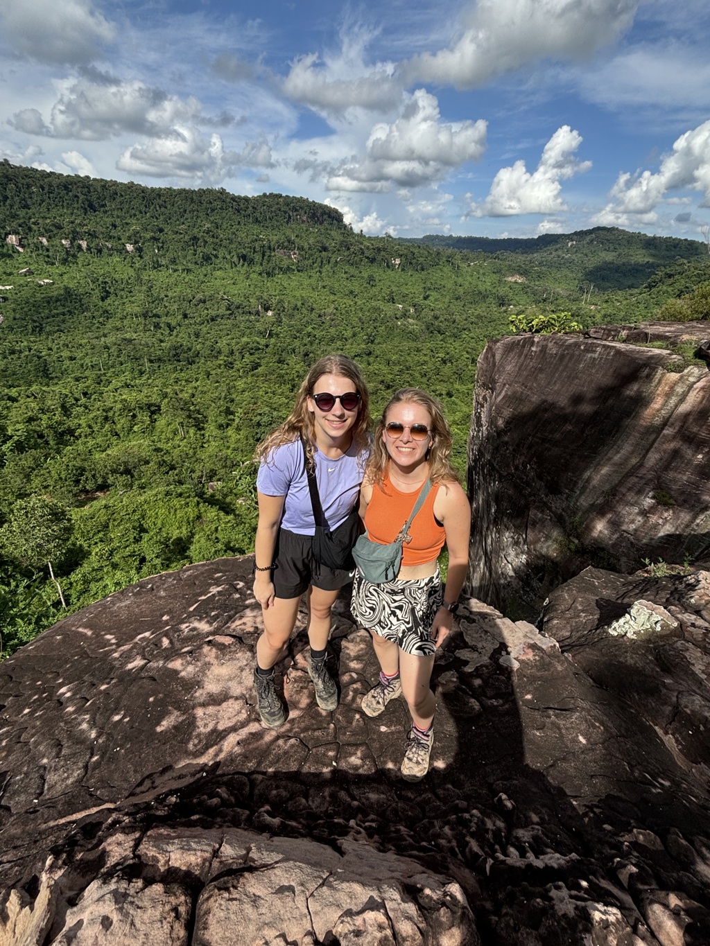Twee reizigers op een rotsplateau met uitzicht op groene jungle en heuvels tijdens 22-35ers reis Thailand, Laos & Cambodja.