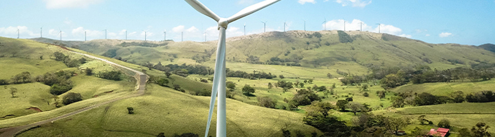 Windmolen in groen heuvellandschap als symbool voor duurzaam reizen en hernieuwbare energie.