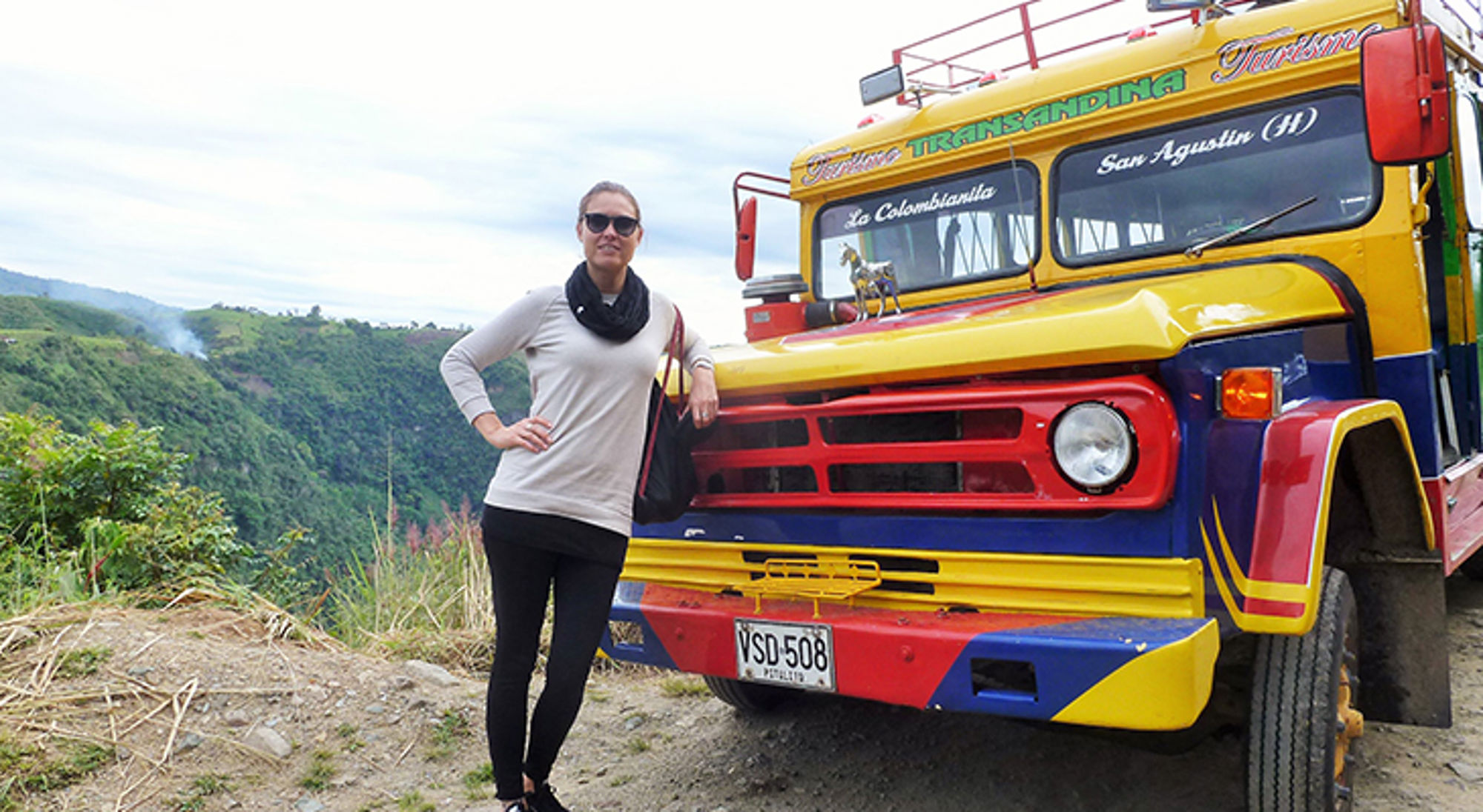 Reiziger poseert bij een kleurrijke Colombiaanse bus in de bergen.