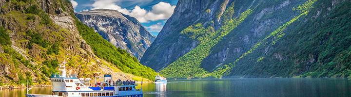 Cruiseschip vaart door een Noorse fjord tussen steile bergen tijdens een rondreis door Scandinavië.