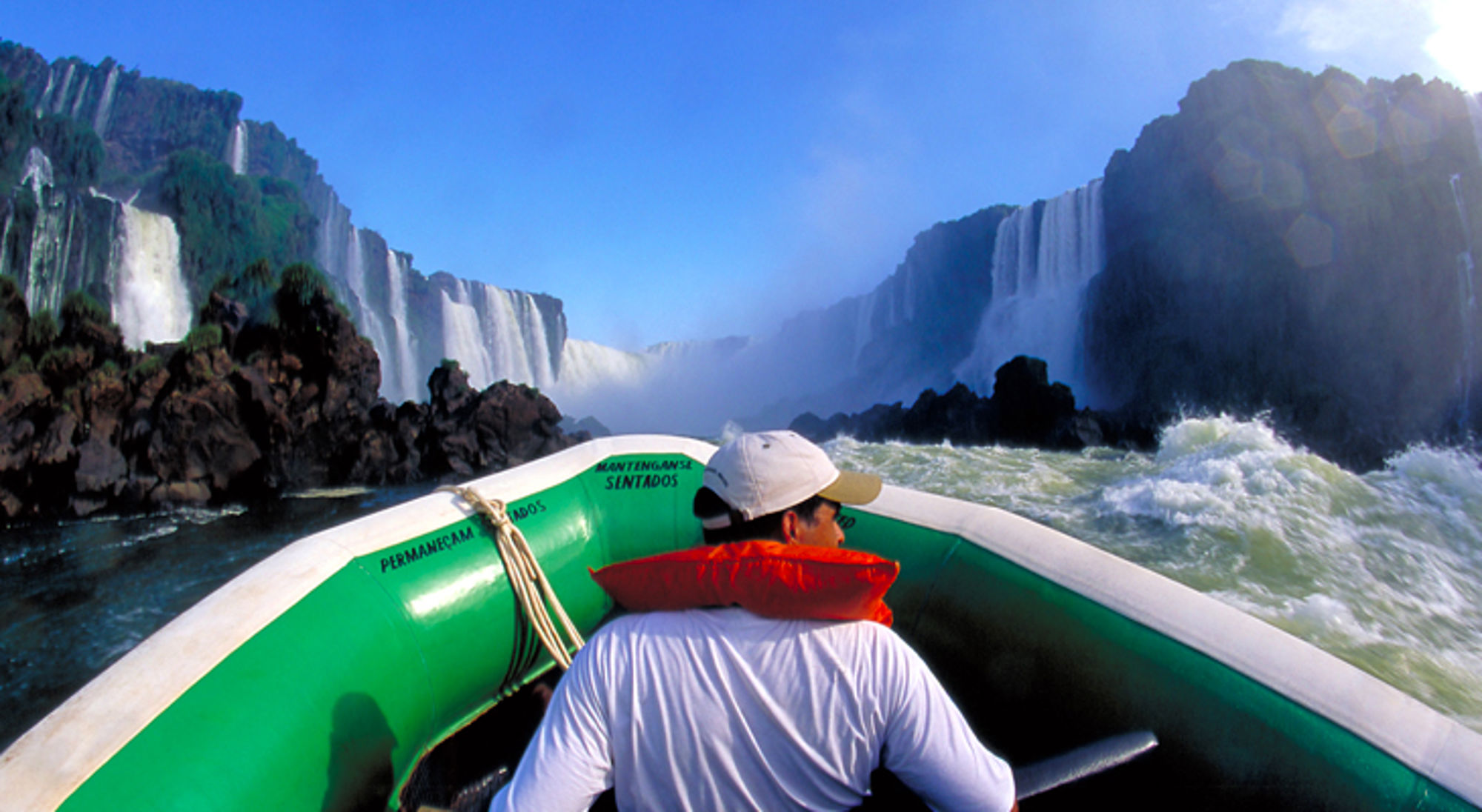Boottocht op de rivier bij de Iguazú-watervallen, met schuimende stroomversnellingen en hoge watervallen op de achtergrond.