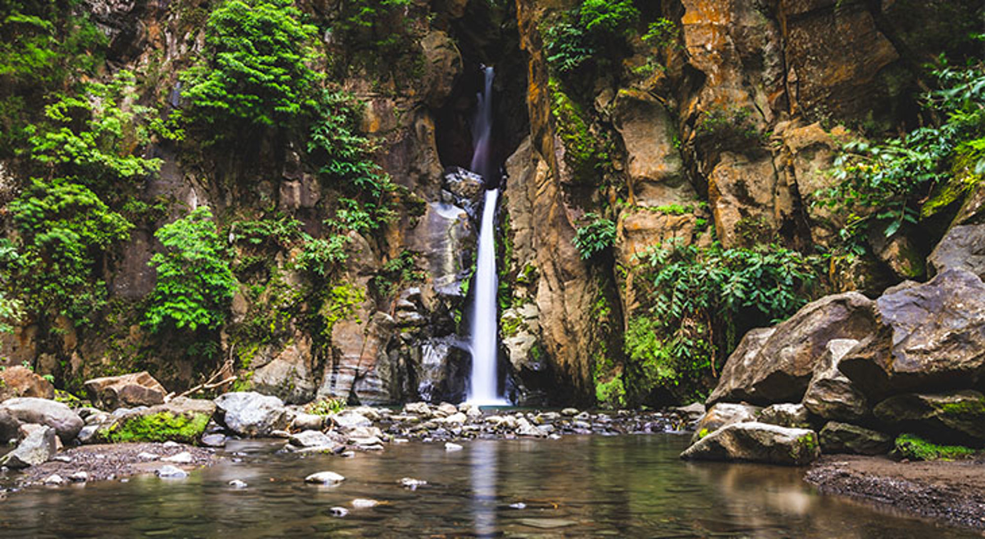 Salto do Cabrito waterval in Portugal Waterval in een rotsachtige kloof met groen begroeiing en een rustige rivier op de voorgrond.