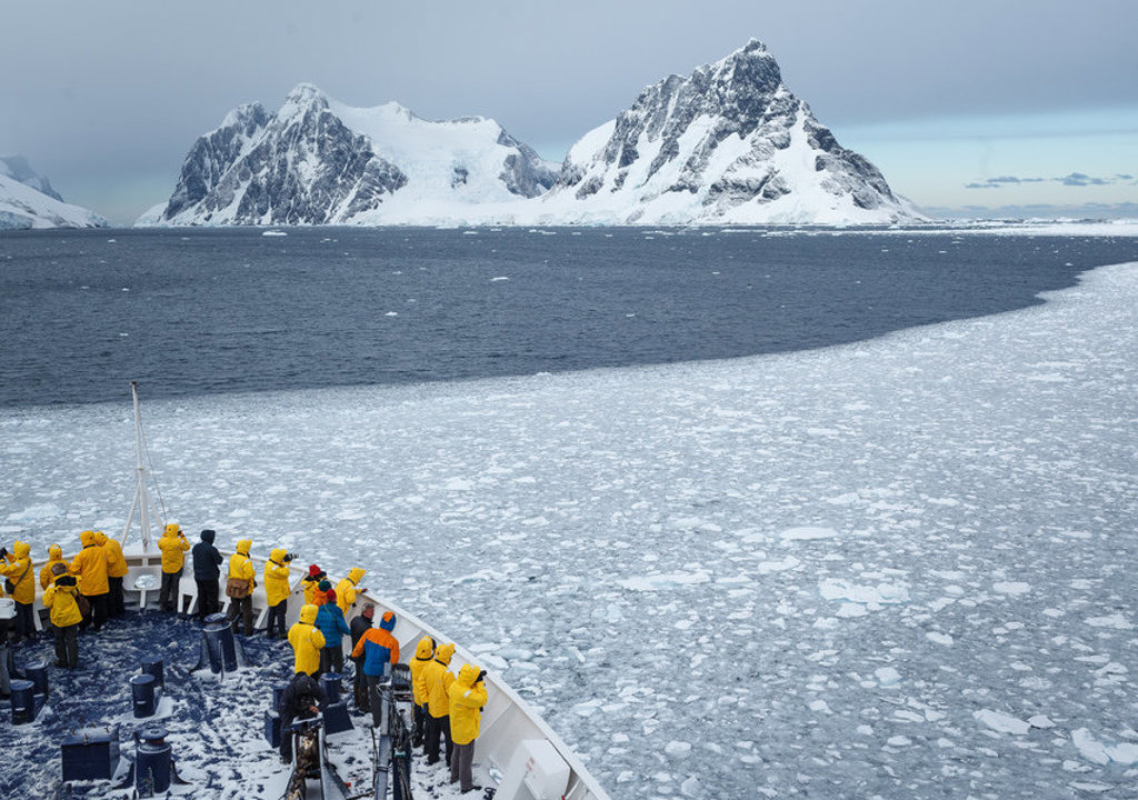 Reizigers op expeditieschip tussen pakijs met besneeuwde bergen in Antarctica.