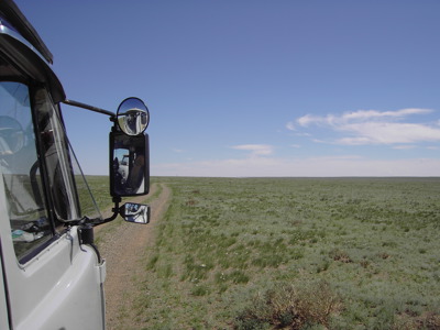 4x4 rijdt over een zandpad door de uitgestrekte Mongoolse steppe onder een blauwe lucht.