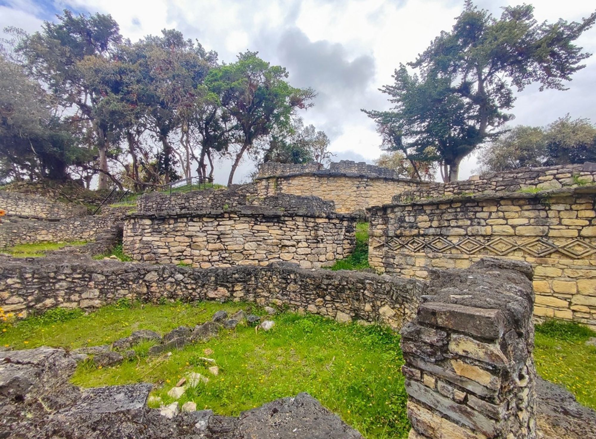 Kuelap-ruïnes in Peru met ronde stenen muren en reliëfpatronen, omringd door groen en bomen.