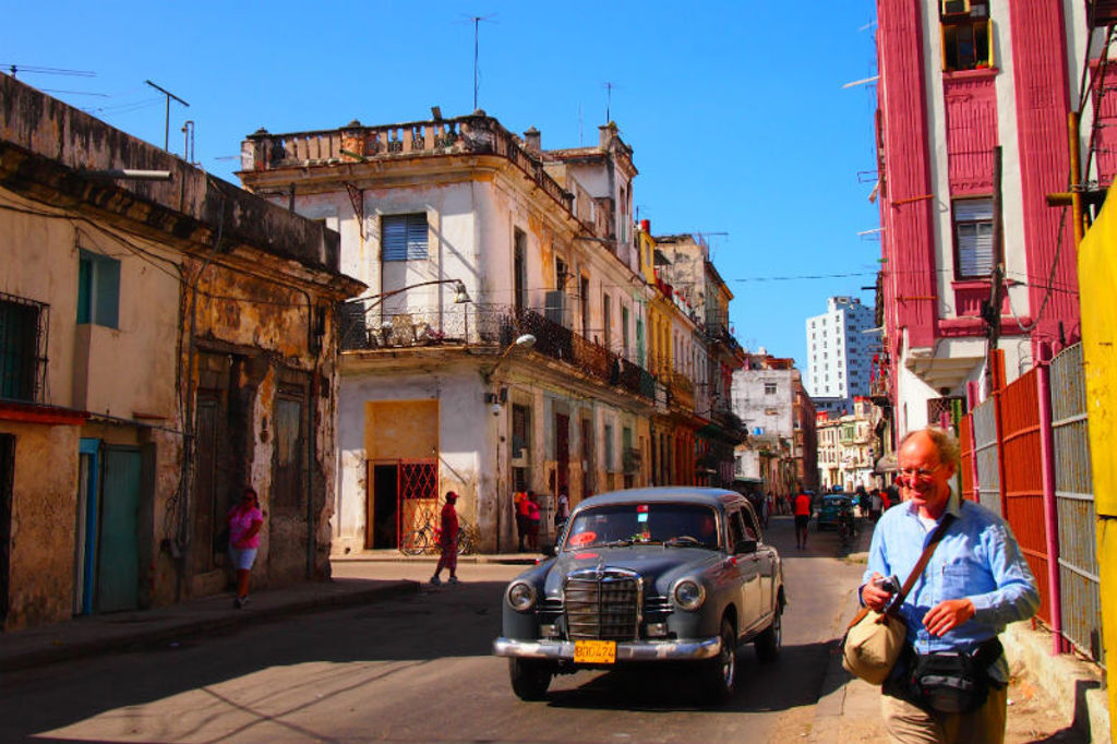 Straat in Havana met kleurrijke gebouwen, een klassieke oldtimer en een reiziger tijdens de familiereis Cuba Hoogtepunten.
