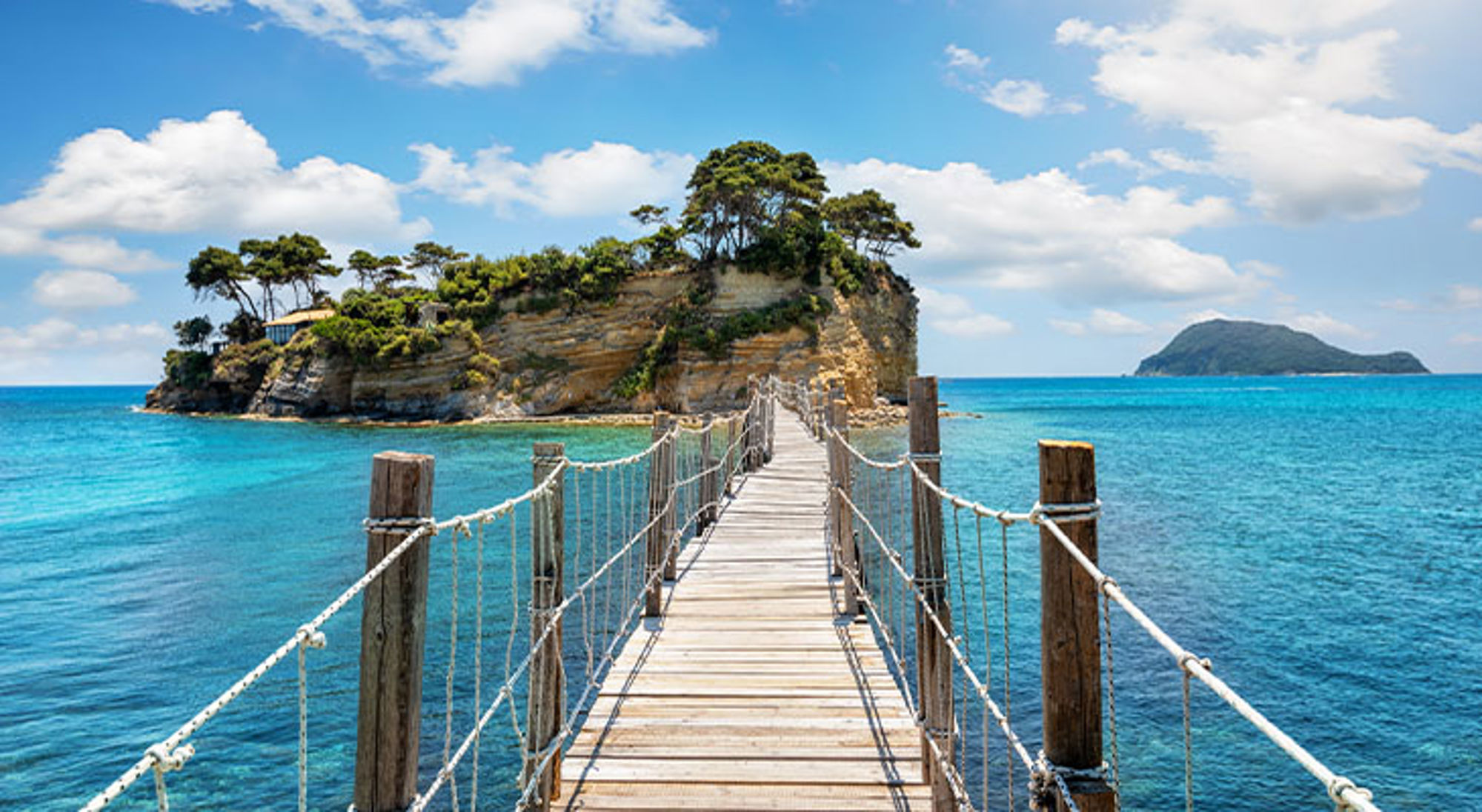 Zakynthos Houten loopbrug naar een groen eilandje in helderblauw zeewater onder een zonnige lucht.