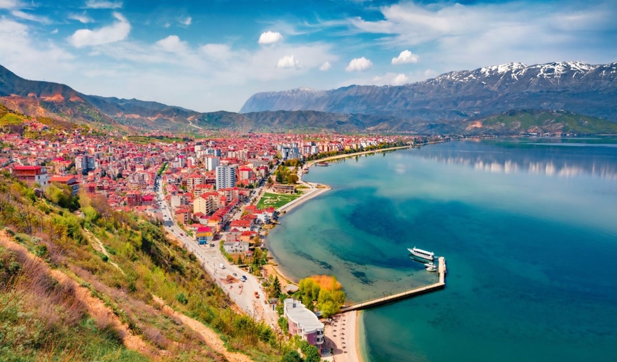 Panorama van Pogradec aan het Meer van Ohrid met boulevard, pier en bergen op de achtergrond.