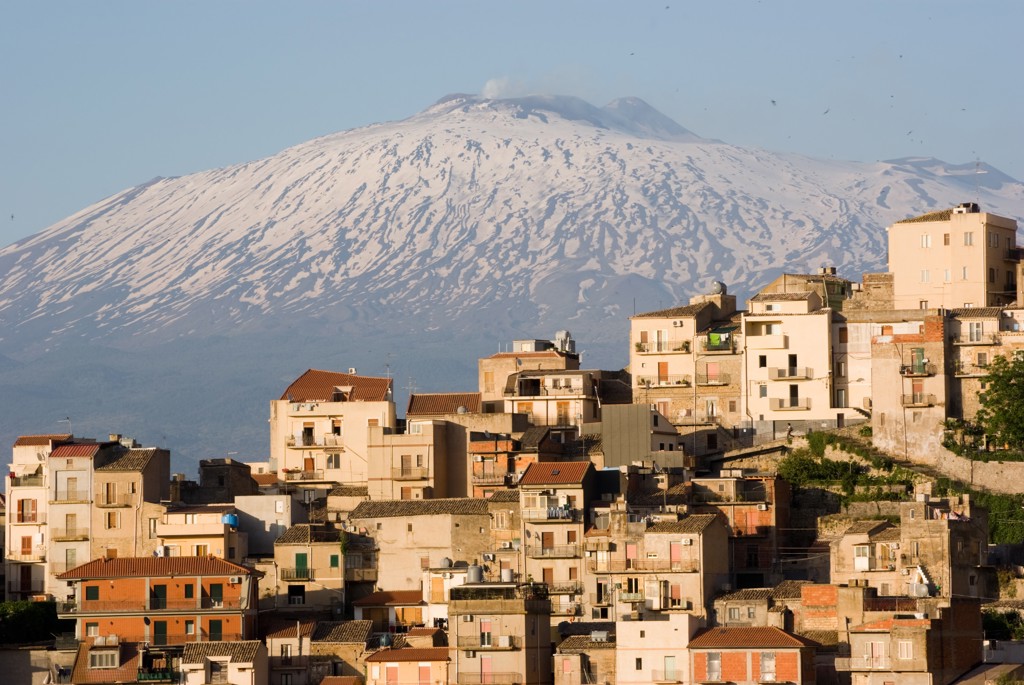 Sneeuw op de Etna boven een Siciliaans dorp met kleurrijke huizen.