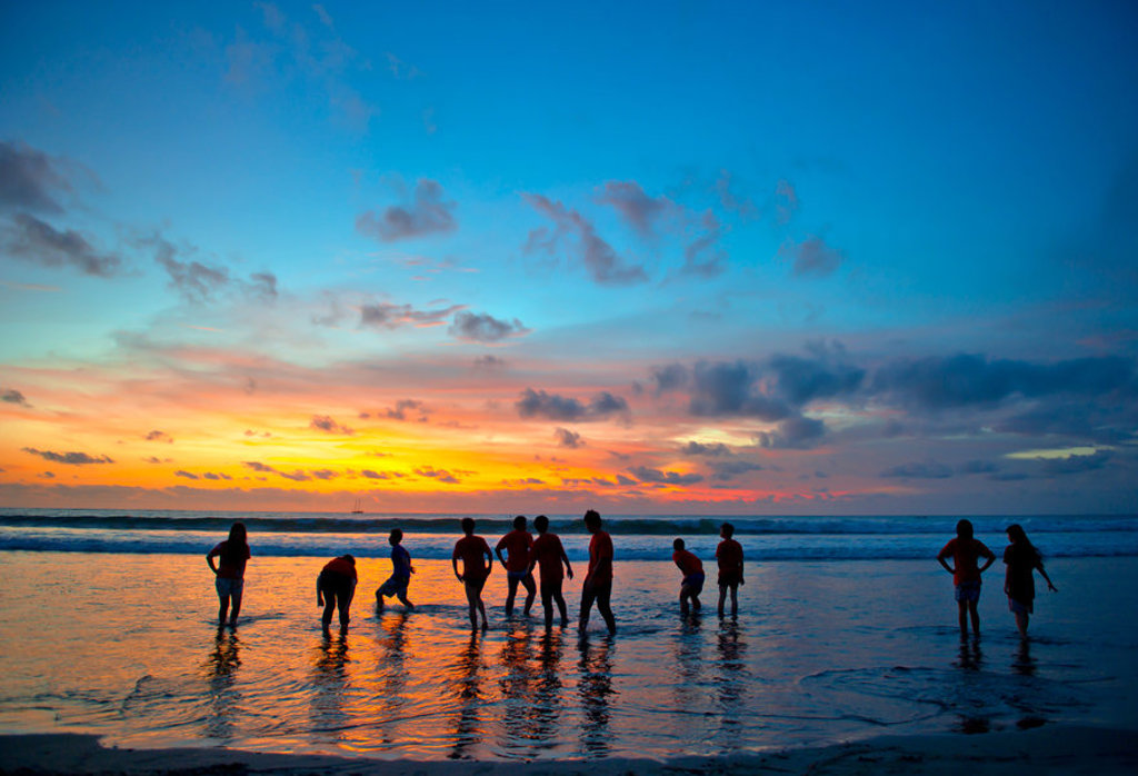 Groep reizigers op het strand bij zonsondergang op Bali tijdens 22-35ers rondreis Indonesië.