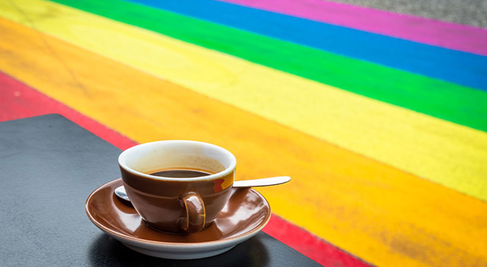 Rainbow street Reykjavik Kop koffie op een tafeltje met op de achtergrond felgekleurde regenboogstrepen.