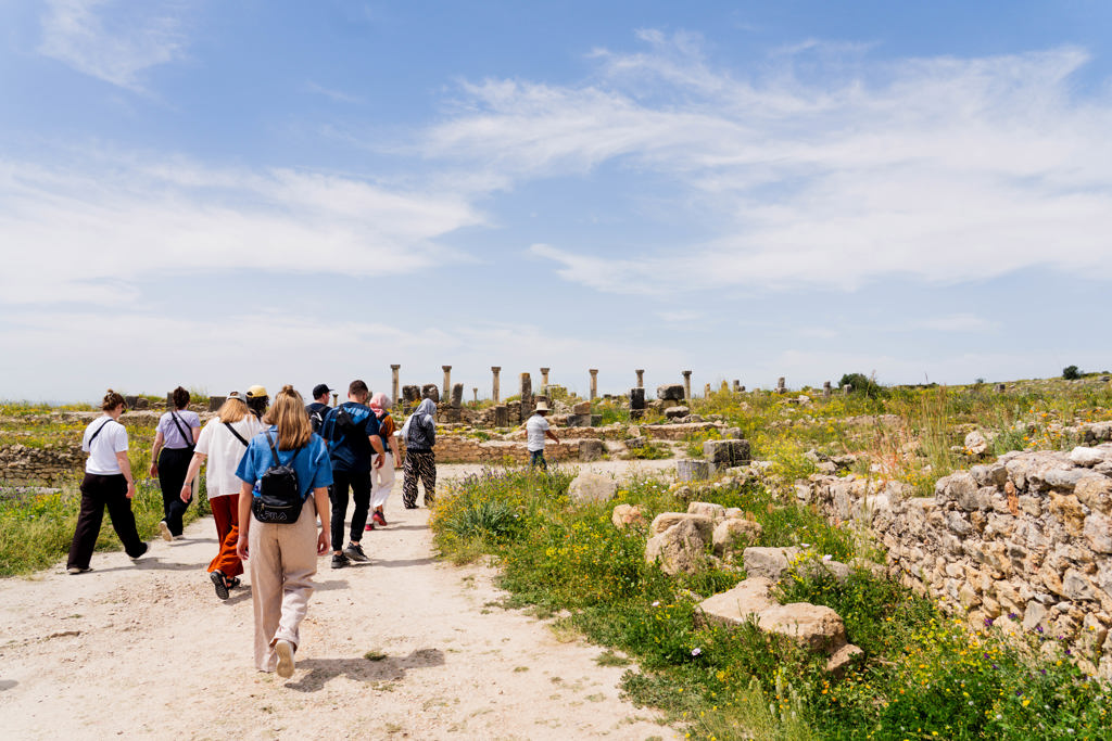 22-35ers groepsreis in Marokko: reizigers wandelen langs ruïnes met zuilen onder een blauwe lucht.