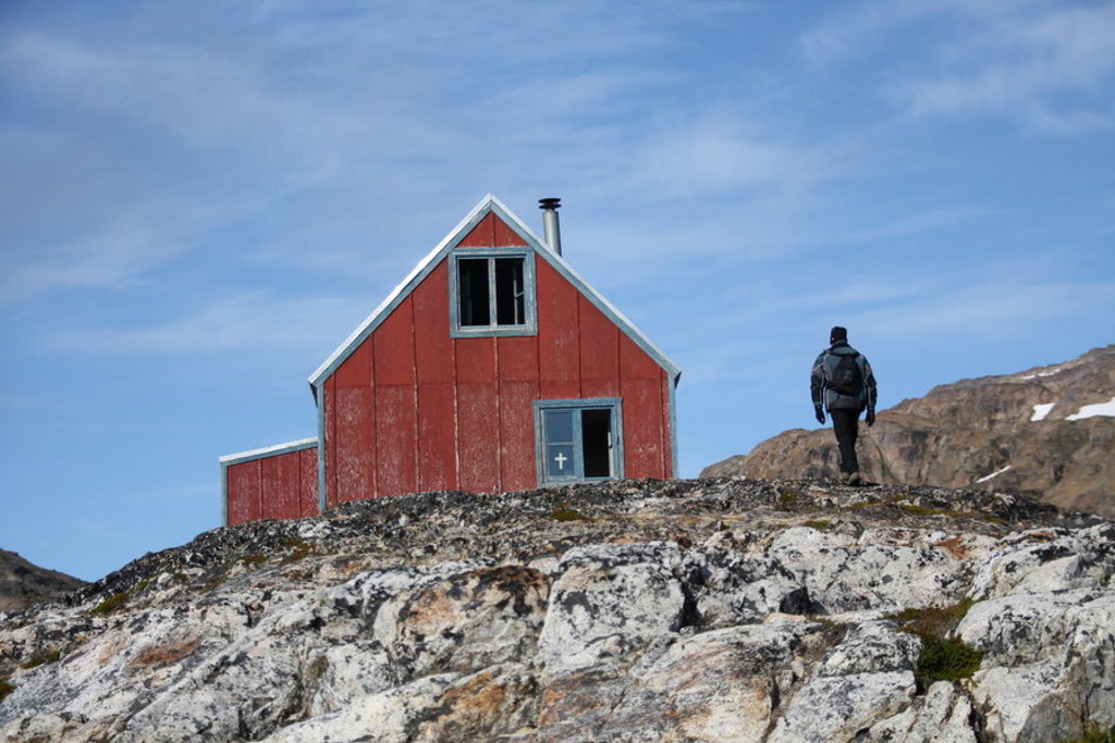 Wandelaar bij rood huisje op rotsachtige heuvel in Disko Bay, Groenland.