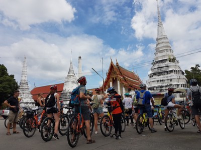 Fietsgroep bij een Thaise tempel met witte stoepa’s en rood-gouden dak onder een blauwe lucht.