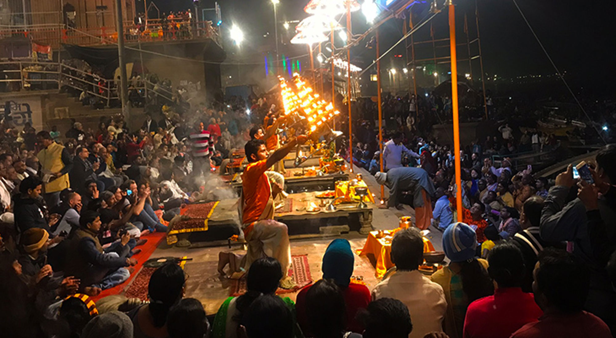Avondceremonie aan de Ganges in Varanasi met priesters en brandende olielampen voor een groot publiek.