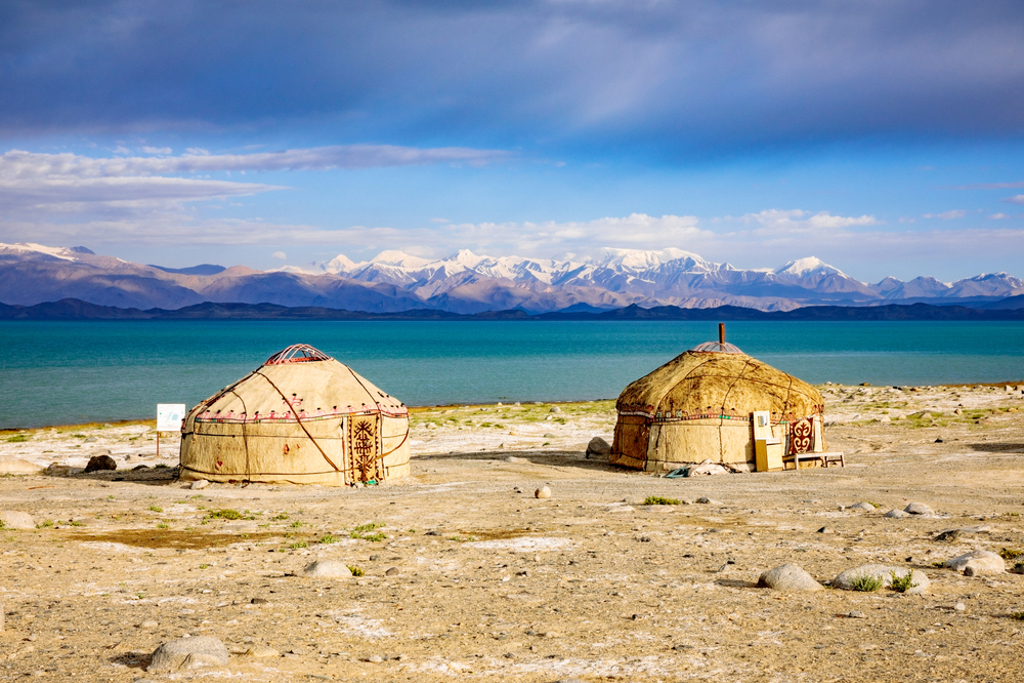 Twee yurts aan een turquoise bergmeer met besneeuwde bergtoppen, tijdens groepsrondreis Zijderoute.
