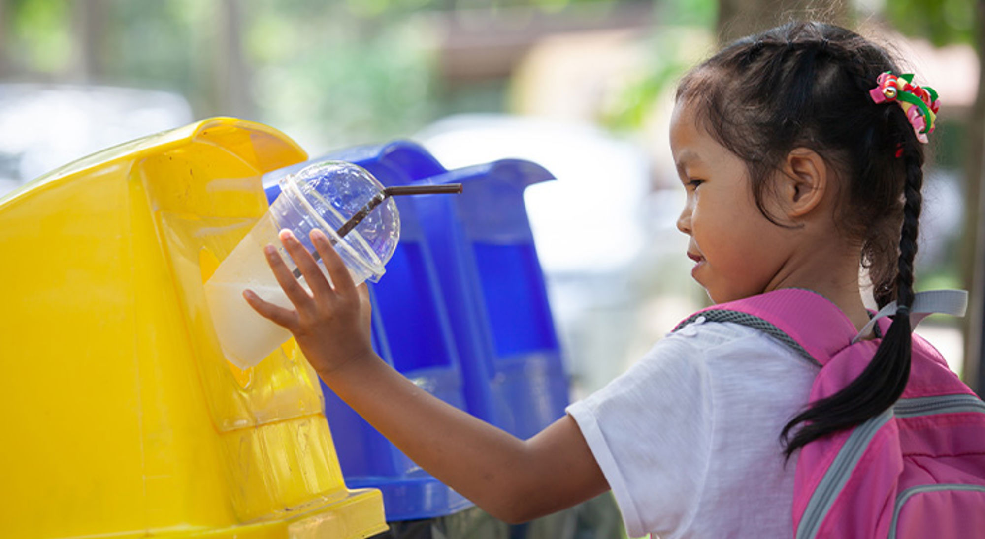 Recyclen op reis Meisje gooit plastic beker in een gele afvalbak voor recycling.