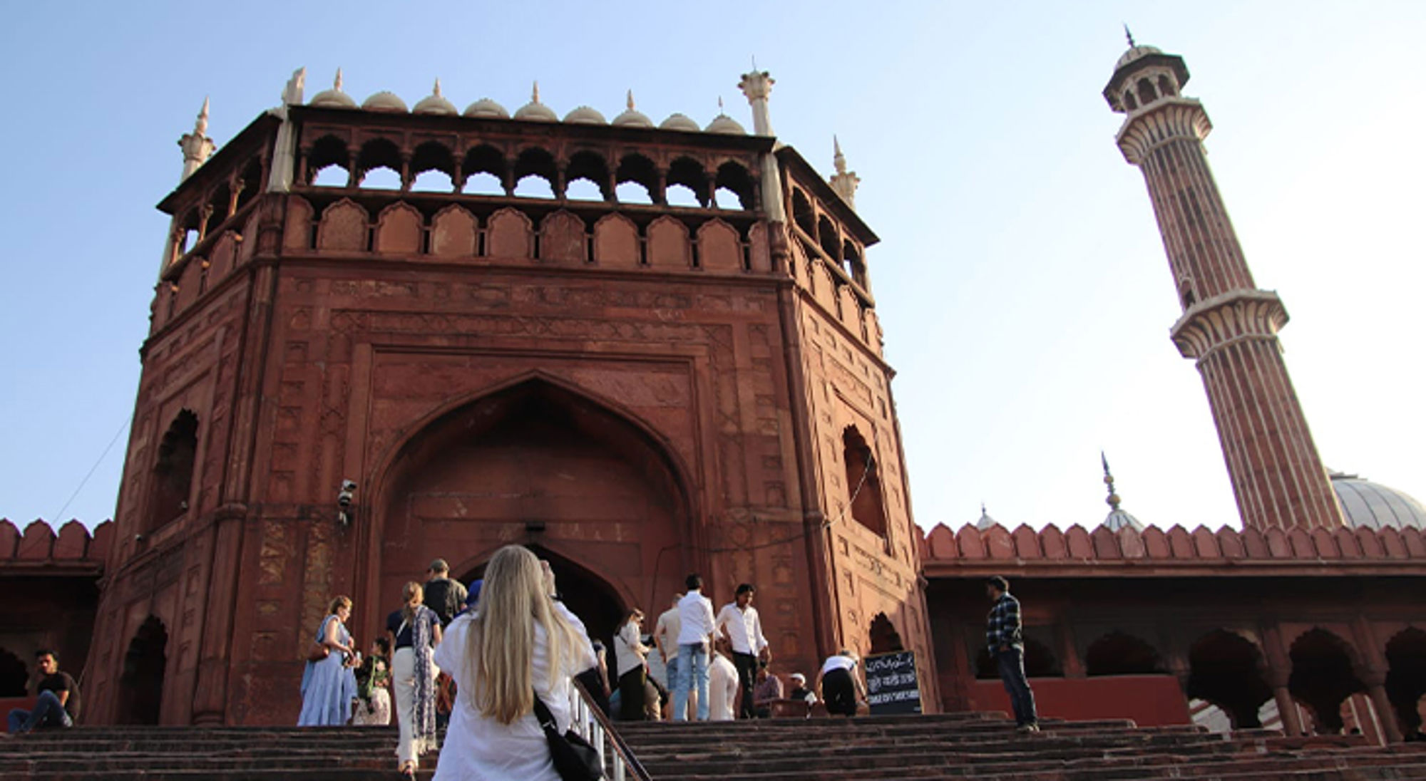 Bezoekers lopen de trappen op naar de rode toegangspoort van de Jama Masjid-moskee in Delhi.