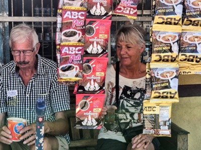 Reizigers bij een lokaal winkeltje op de Kleine Sunda Eilanden, met hangende zakjes koffie en snacks.