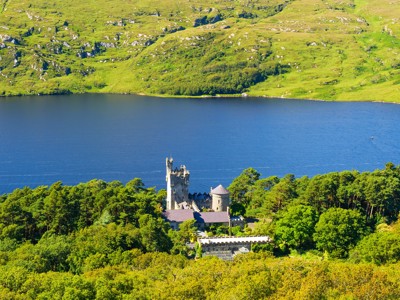 Kasteel aan de oever van een loch, omringd door groen heuvellandschap in Schotland.