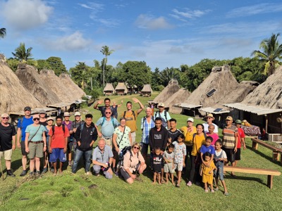 Groepsfoto van reizigers en locals bij traditionele rieten huizen op de Kleine Sunda Eilanden, Indonesië.
