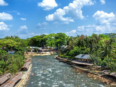Rivier met oeverdorp en tropisch groen langs de route Sumatra, Java en Bali.