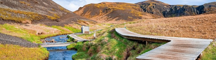 Houten wandelpad langs een beek in de Reykjadalur-vallei, IJsland.