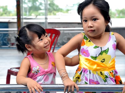 Twee lachende meisjes in kleurrijke jurkjes op een terras tijdens de Route Vietnam.
