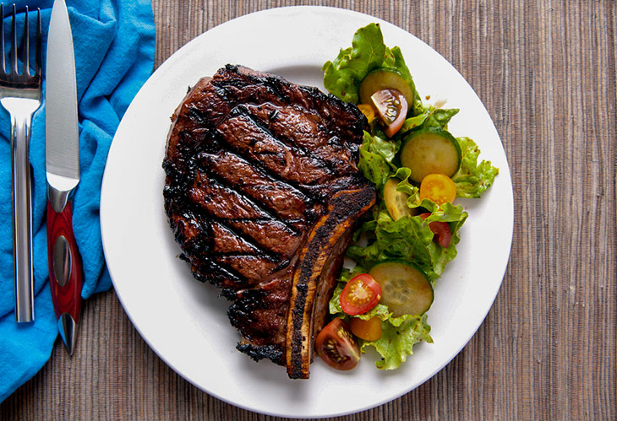 Steak eten in de Verenigde Staten Gegrilde ribeye steak met groene salade en cherrytomaten op een wit bord.