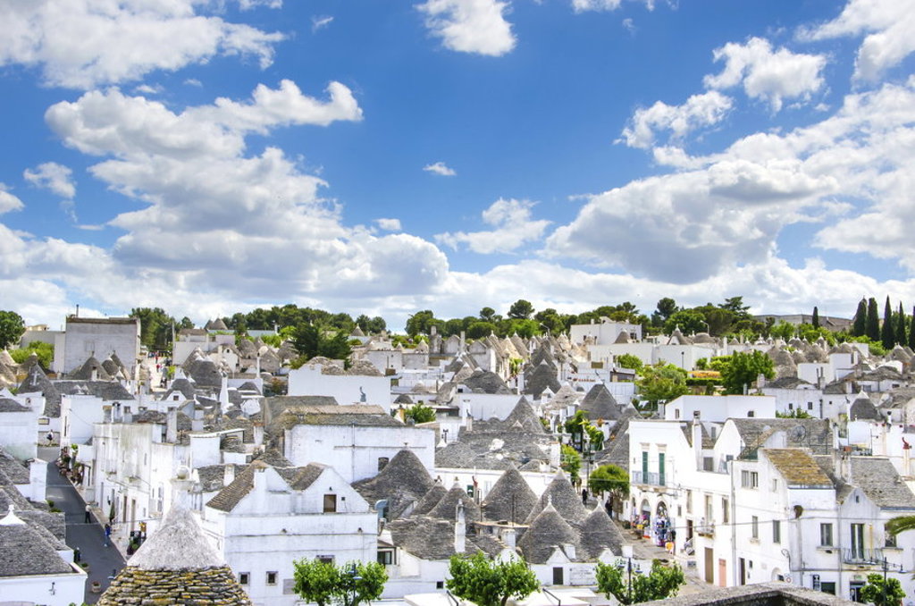 Panorama van Alberobello in Puglia met witte trulli-huisjes en kegelvormige daken onder een blauwe lucht.