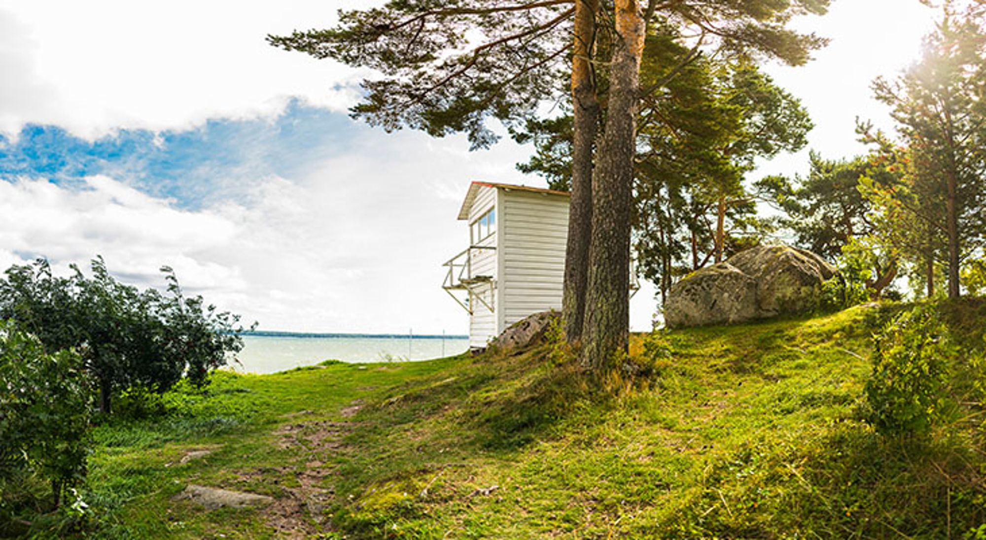 Kasmu Witte vuurtorenwachterswoning aan de kust, omringd door dennenbomen en rotsen.
