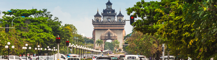 Patuxai-monument in Vientiane, Laos, aan een brede boulevard met verkeer en groene bomen.