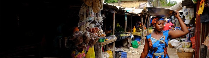 Vrouw met schaal op haar hoofd loopt langs een kleurrijke markt in Senegal.