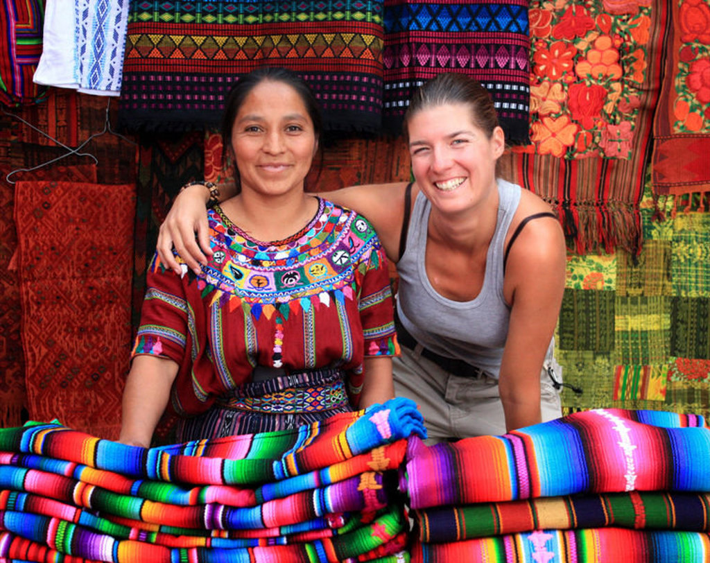 Reiziger poseert met marktvrouw tussen kleurrijke textiel en dekens tijdens groepsrondreis Mexico, Guatemala en Honduras.