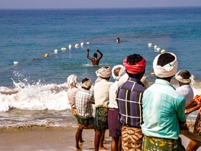 Vissers trekken samen een net aan land op het strand in Zuid-India, met de zee op de achtergrond.