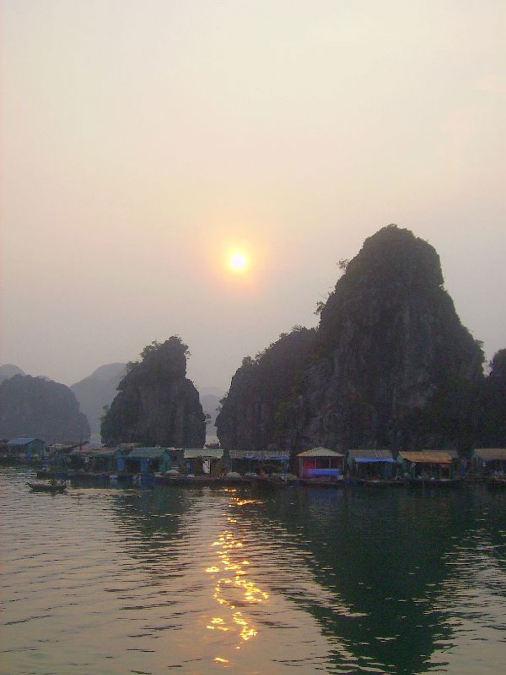 Zonsondergang boven Halong Bay met kalkstenen rotsen en drijvende huisjes in Vietnam.