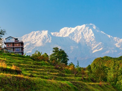 Uitzicht op de besneeuwde Himalaya bij Pokhara, Nepal, met groen heuvellandschap en lodge op de voorgrond.