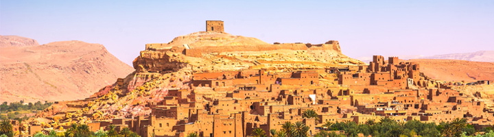 Kasbah Aït Ben Haddou in Marokko, lemen stad op een heuvel met palmoase en bergen op de achtergrond.