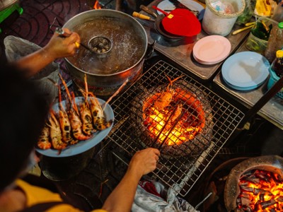 Streetfoodkraam in Thailand met garnalen op houtskoolgrill en kok die een kom klaarmaakt.